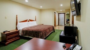 Ein Hotelzimmer mit einem Bett, einem Schreibtisch mit Telefon, einem an der Wand befestigten Fernseher und einem Spiegel.