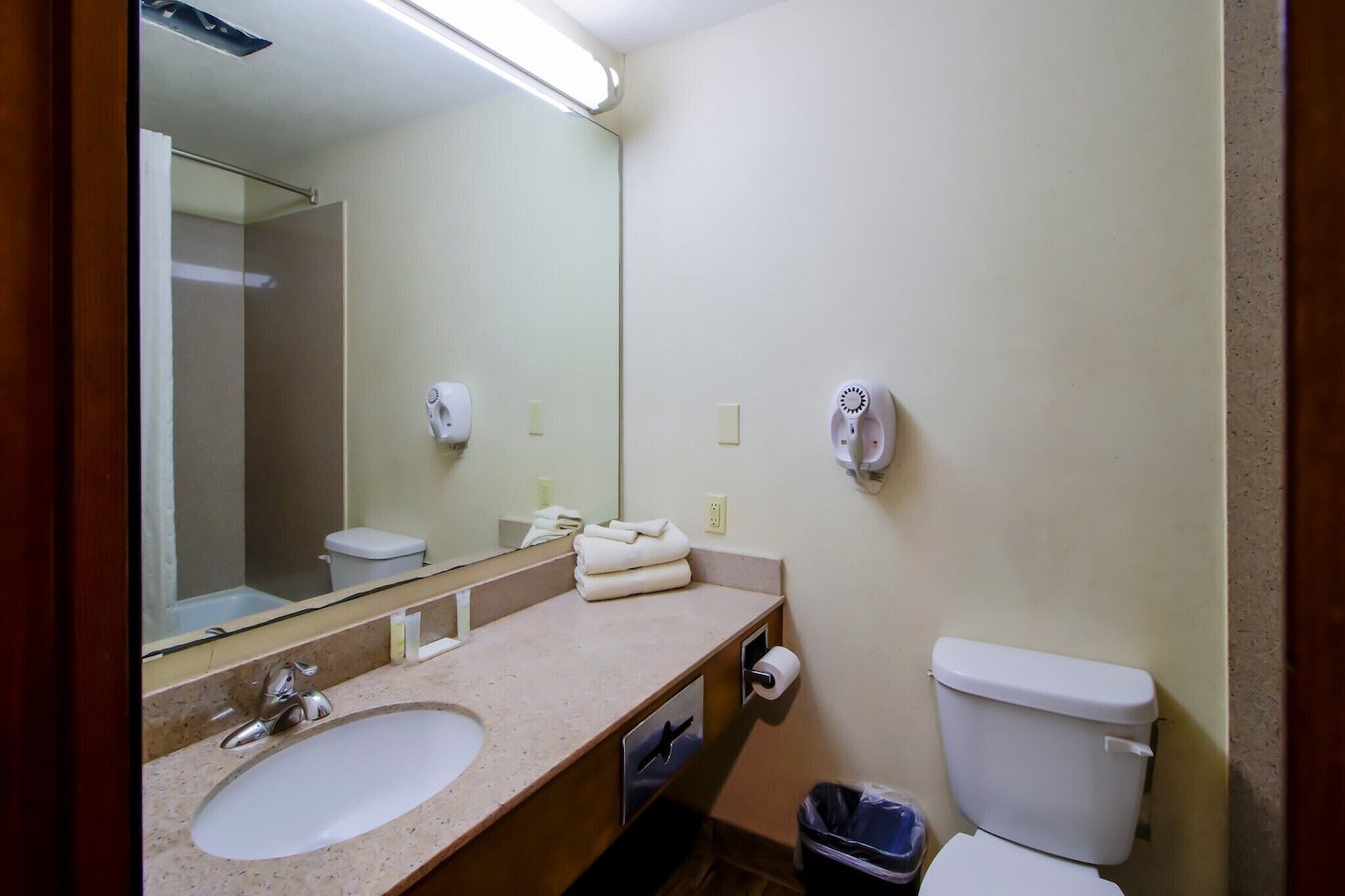 A bathroom with a sink, mirror, towel dispenser, and toilet.