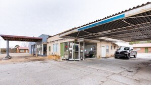 Una estación de servicio con un cartel claro que indica una oficina, una bomba de combustible y un vehículo estacionado.