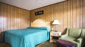 A room with a bed, a nightstand, a chair, and a wall-mounted clock.
