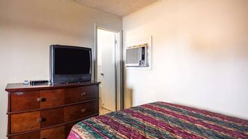 A bedroom with a bed, a dresser, a television, and an air conditioning unit.