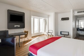 Ein Hotelzimmer mit Bett, Schreibtisch, Stuhl, Fernseher und einer Küchenzeile.