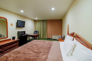 Ein Hotelzimmer mit einem Bett, einem Schreibtisch, einem Fernseher, einem Spiegel und einem Fenster mit Vorhängen.