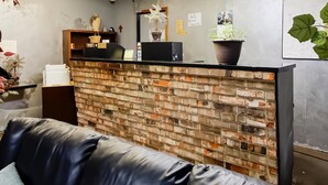 Ein Empfangsschalter mit einer Backsteinwand, einer schwarzen Ledersofa und einem Blumentopf.