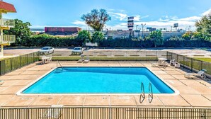 Une piscine rectangulaire dotée d’un plongeoir, entourée d’une clôture et de chaises longues.