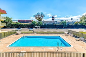 A rectangular pool with a diving board, surrounded by a fence and lounge chairs. - Houston | 2 Full Bed (Houston)