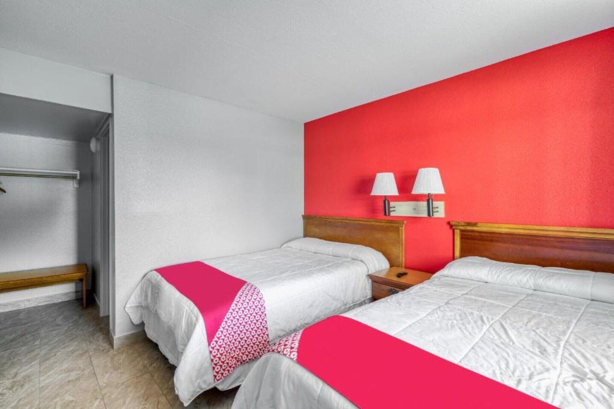 Camera d'albergo con due letti, una panca, un comodino e una parete decorata di rosso.