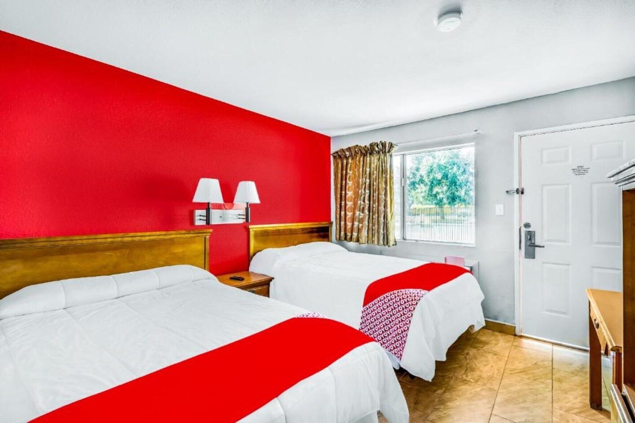 A hotel room with two beds, a window with curtains, a door, and a nightstand with lamps.