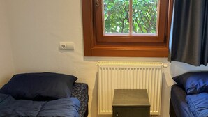 A bedroom with two beds, a radiator, and a window with a view of greenery. - Holiday Home in Susteren With Terrace (Susteren)