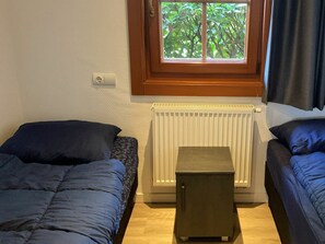 Ein Schlafzimmer mit zwei Betten, einem Heizkörper und einem Fenster mit Blick auf Grünflächen.