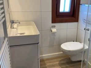 Ein Badezimmer mit weißem Waschbecken, Toilette und einem kleinen Fenster über der Toilette.