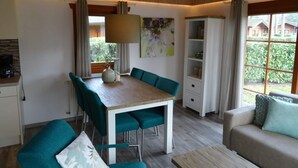 A dining area with a wooden table and teal chairs, a sofa with a cushion, and a window with a view of greenery. - Holiday Home in Susteren With Terrace (Susteren)