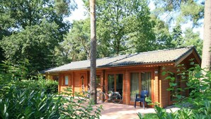 A wooden cabin with a covered porch, bicycles, and a number 134 sign. - Holiday Home in Susteren With Terrace (Susteren)