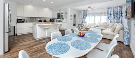 Een moderne keuken met witte kasten, een centraal eiland en een eethoek met een witte tafel en stoelen.