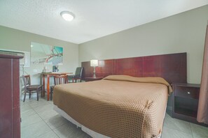 A hotel room with a bed, a desk with a chair, a lamp, and a painting on the wall.