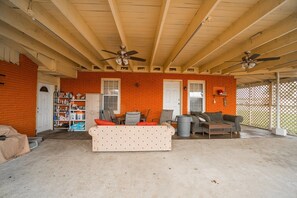 A covered outdoor living area with a brick wall, ceiling fans, a sofa, and a trash can.