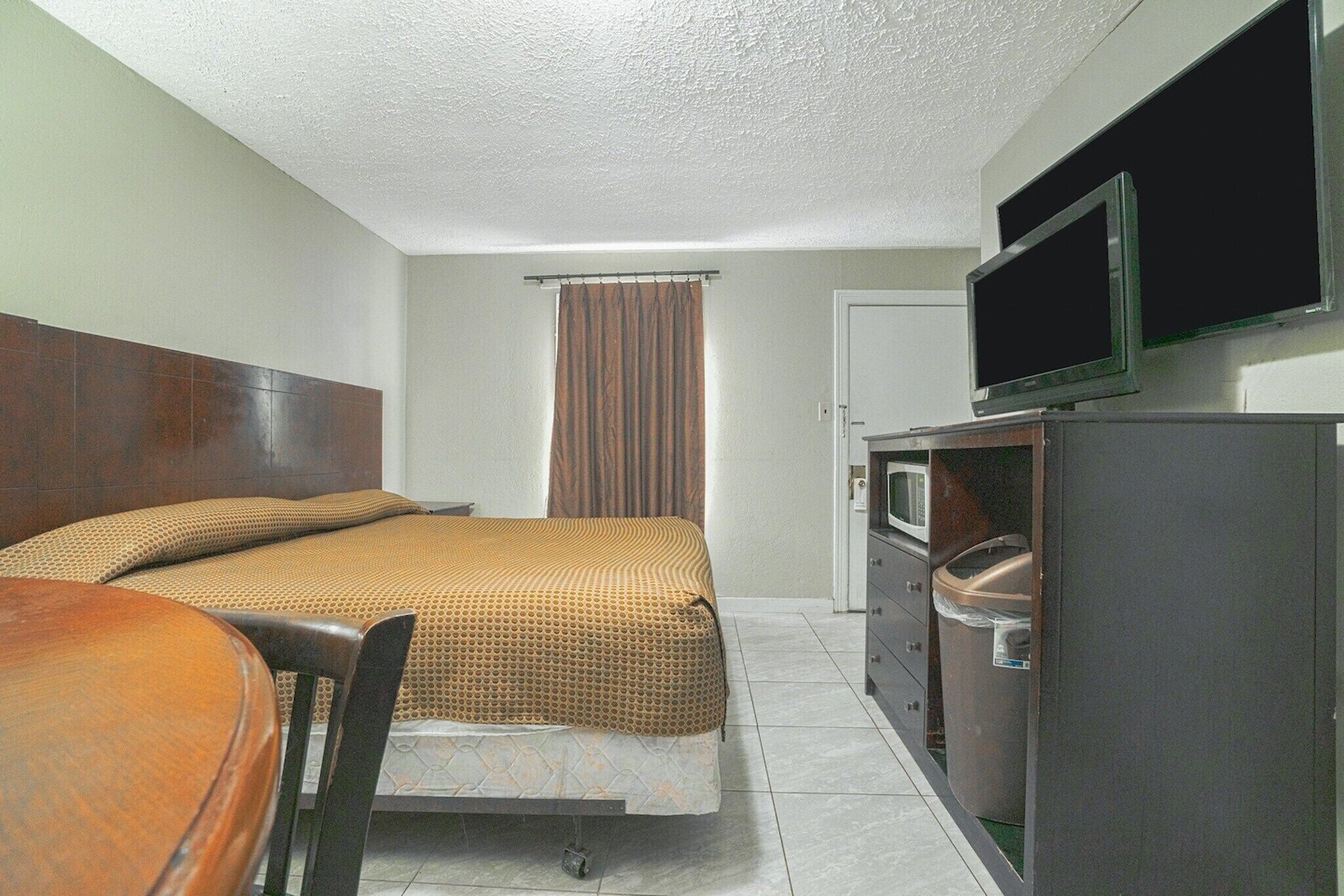 Una habitación de hotel con cama, escritorio, silla, televisor y microondas.