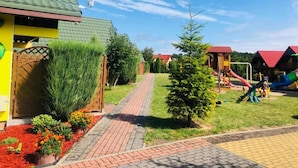Ein Wohngebiet mit einem Weg, der zu einem Haus mit Gründach, einem kleinen Baum und einem Spielplatz mit Rutschen führt.