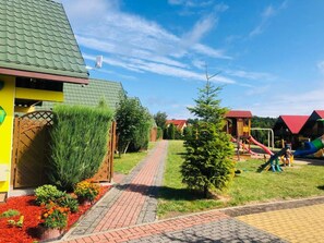 Ein Wohngebiet mit einem Weg, der zu einem Haus mit Gründach, einem kleinen Baum und einem Spielplatz mit Rutschen führt.