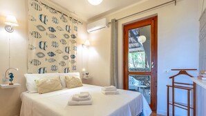 Ein Schlafzimmer mit einem Bett, Nachttischlampen, einer Wand-Klimaanlage und einer Holztür zu einem Außenbereich.