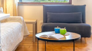 Ein Zimmer mit einem Bett, einem Sessel, einem kleinen Tisch mit einem Buch und zwei Tassen sowie einem Fenster mit Blick.