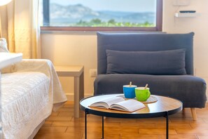 Una stanza con un letto, una sedia, un tavolino con un libro e due tazze, e una finestra vista.