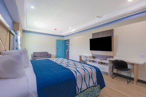 Habitació d'hotel amb llit, escriptori, cadira, televisió i una porta.