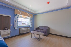 A room with a bed, a table, a sofa, a window with curtains, a heater, and a wall-mounted phone. - King Bed with Kitchenette Non-Smoking (Houston)