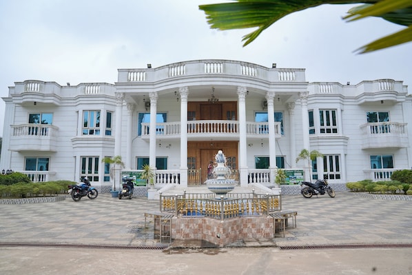 A large, white building with a central fountain, multiple balconies, and a symmetrical facade.