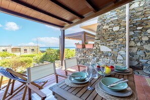 Un terrazzo in legno con un tavolo apparecchiato per mangiare, affacciato su un muro in pietra e vista sull'oceano.