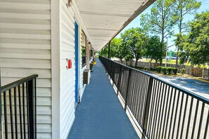A covered corridor with a blue floor, metal railing, and a row of buildings with visible doors and windows. - King Bed Smoking | Albany (Albany GA)