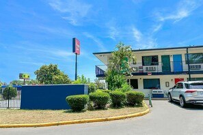 A motel with a two-story structure, a fenced parking area, and a car parked in front. - King Bed Smoking | Albany (Albany GA)