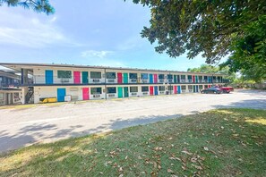 A motel with multiple colorful doors, a parking lot, and a grassy area. - King Bed Smoking | Albany (Albany GA)