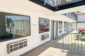 A row of single-story buildings with large windows, a sign indicating an office, and a red vehicle parked outside.