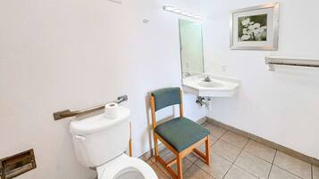 A bathroom with a toilet, a sink, a chair, a mirror, and a framed picture on the wall.