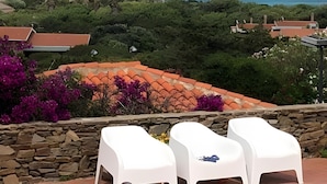 Vista a la piscina con sillones, un muro de piedra y el océano con veleros.