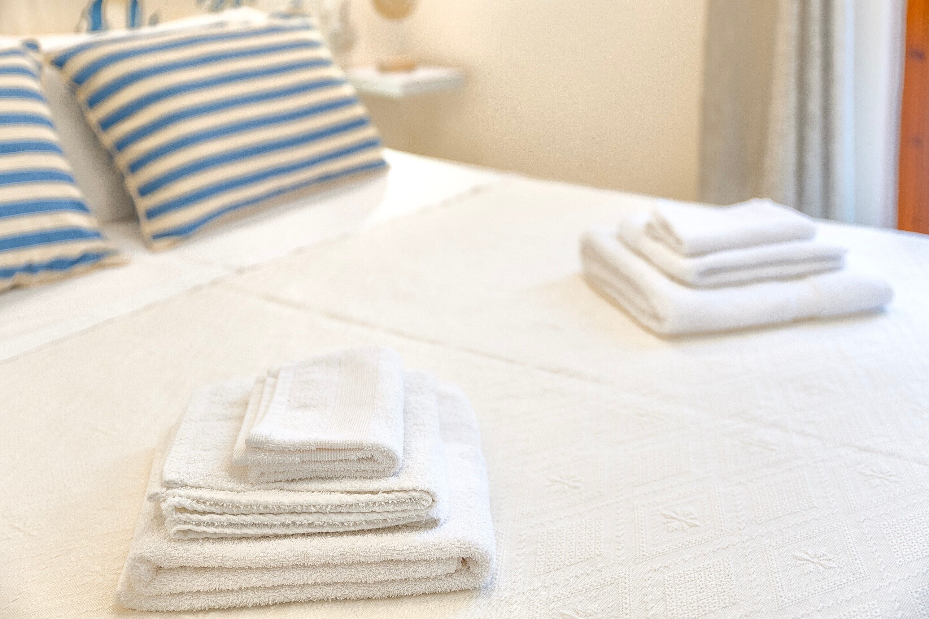 A neatly made bed with white and blue striped pillows and folded white towels.