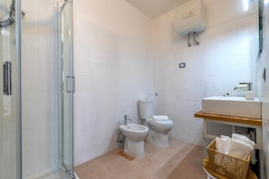 Un bany amb una cabina de dutxa de vidre, un vàter, un lavabo i una cistella per a tovalloles.