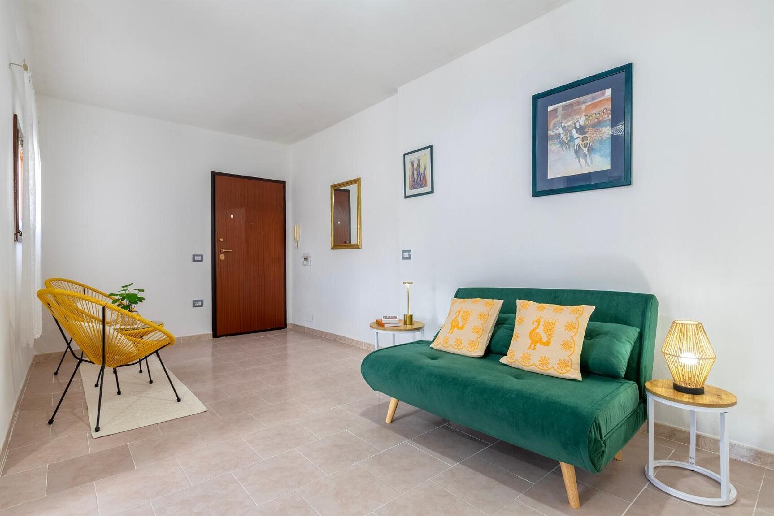 A room with a green sofa, a yellow chair, a small side table with a lamp, and a door.