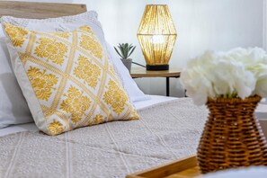 Ein Bett mit einem gemusterten Kopfkissen, einer Lampe, einer kleinen Pflanze und einer Vase mit Blumen.