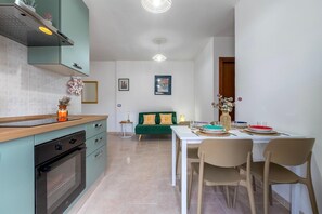 Een moderne keuken met een inbouwoven, een eettafel met stoelen en een groene bank op de achtergrond.