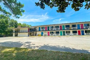A motel with a row of rooms, each with a different colored door, and a parking lot in front.