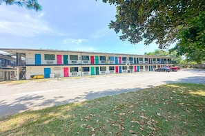 Un motel con varias puertas de colores, un estacionamiento y una zona con césped.