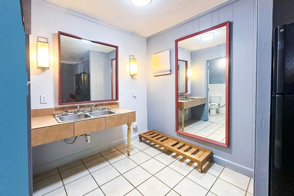 A bathroom with two sinks, a wooden shelf, and a mirror with a red frame.