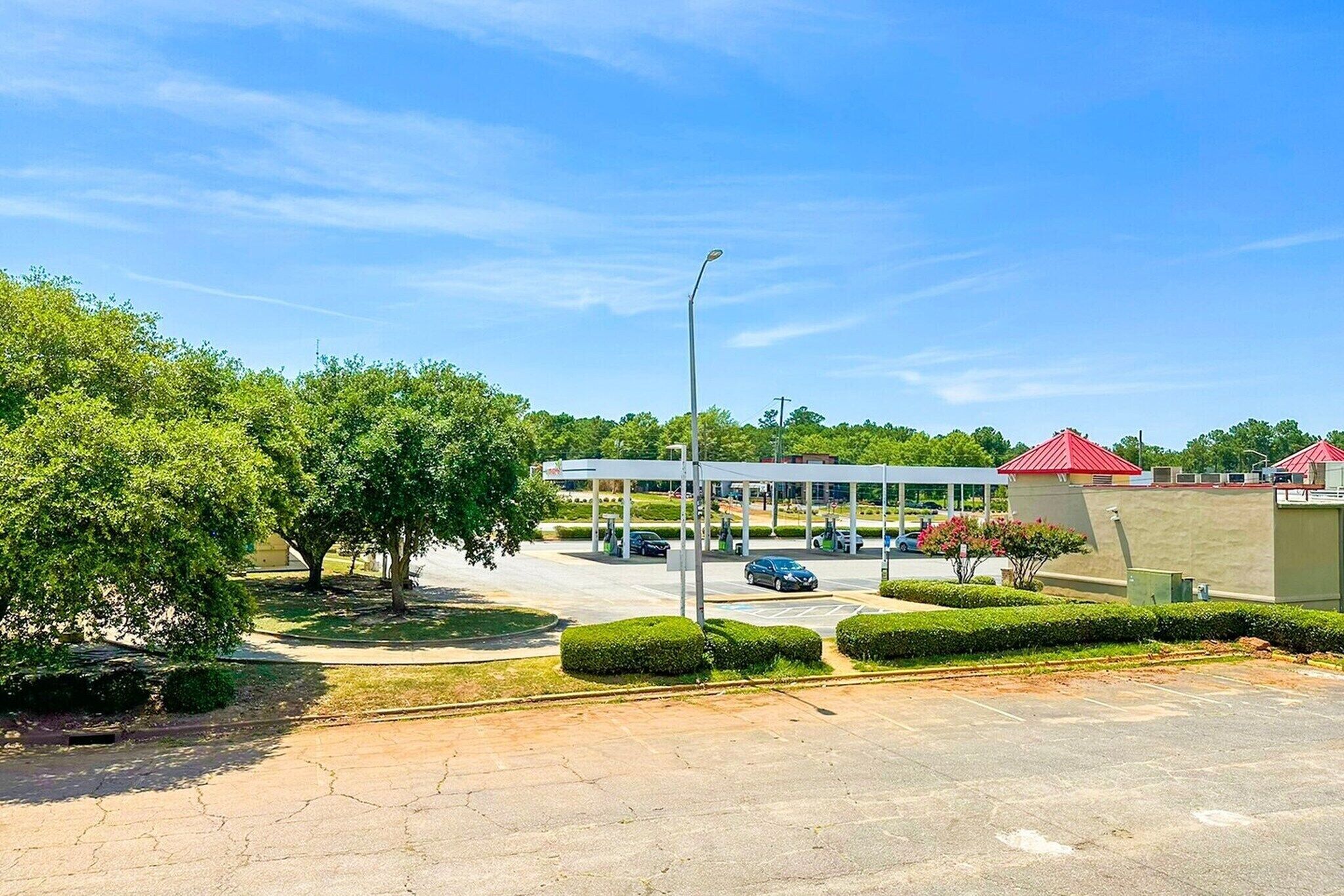 Una estación de servicio con varias bombas de combustible, un área de estacionamiento techada y un edificio con tejados rojos.