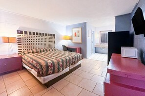 Ein Schlafzimmer mit Bett, Nachttischen, einer Lampe, einem gerahmten Bild, einem Fernseher und einer Mikrowelle.