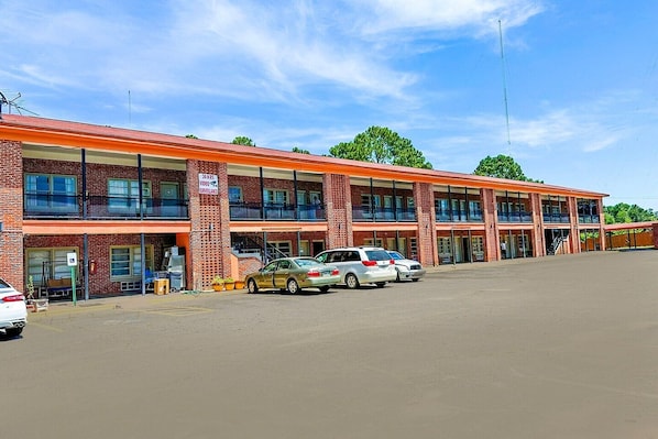 Un motel de varios pisos con fachada de ladrillo, varios balcones y un estacionamiento con varios automóviles.
