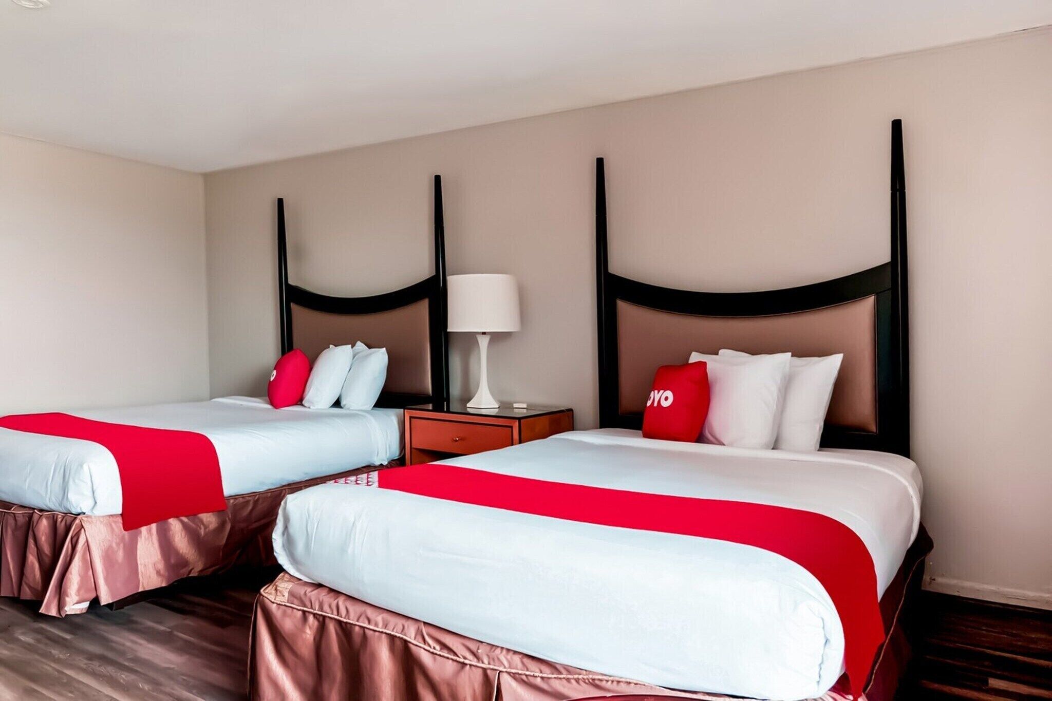 Twee bedden met rood-witte beddengoed, een nachtkastje met een lamp, en een muur met een verticaal zwart design.