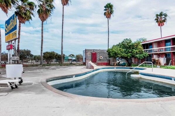 A pool area with a small building, palm trees, and a sign for Scottish Inns. - 3 Queen Bed | Non Smoking (Alice TX)