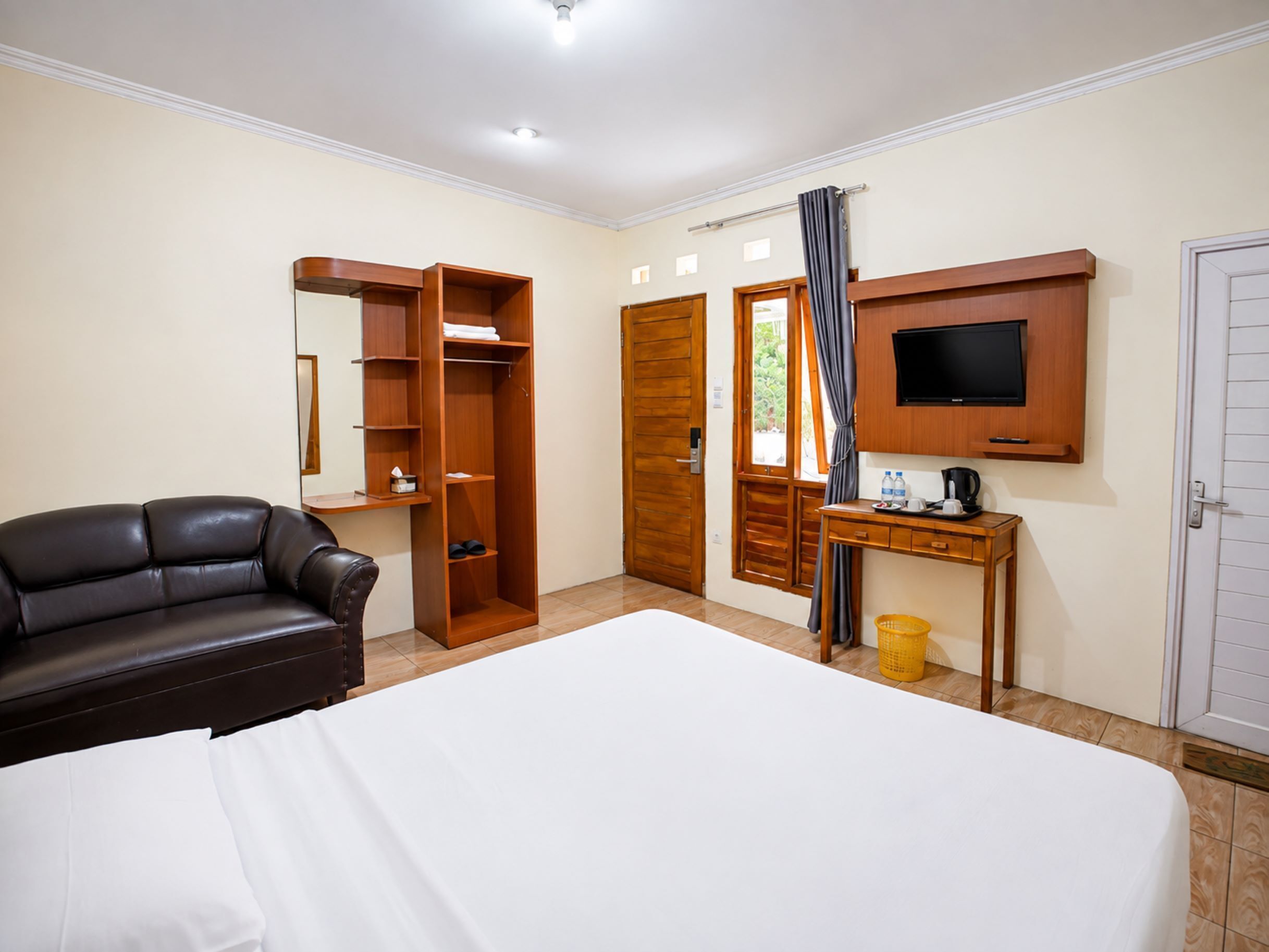 A hotel room with a bed, a desk with a TV, a wardrobe, and a leather sofa.